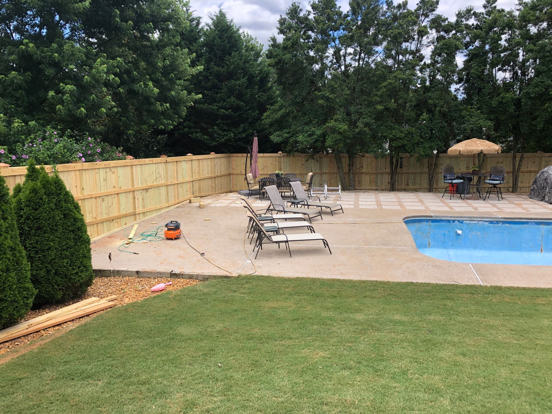Backyard with pool, patio, wooden fence, lounge chairs, and green lawn.