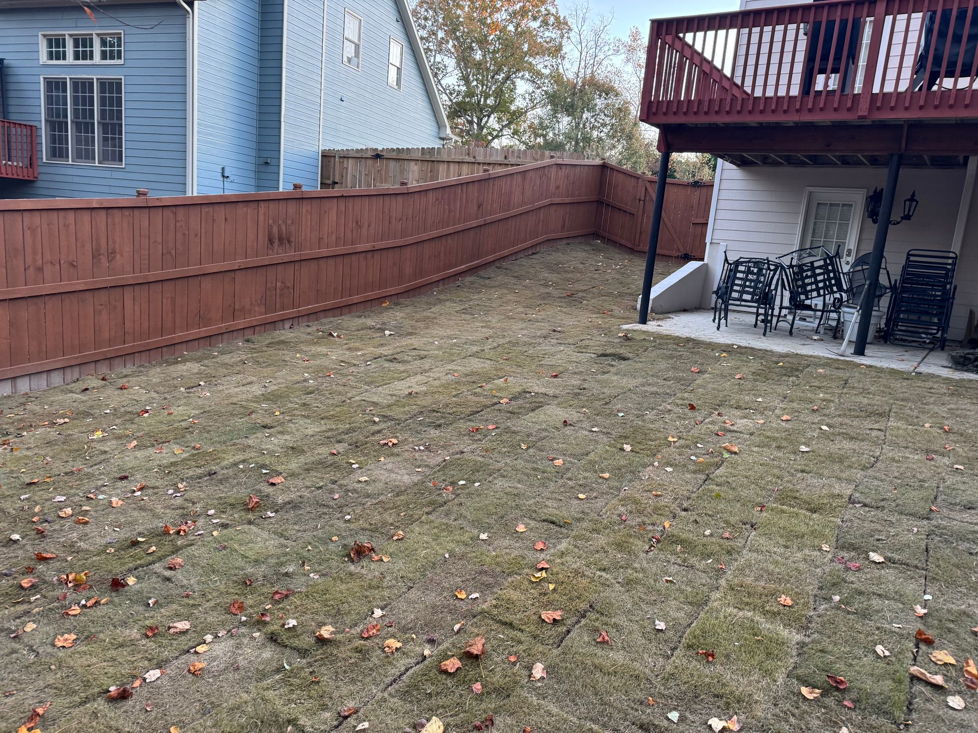 Brown fenced backyard with dry grass and a deck.
