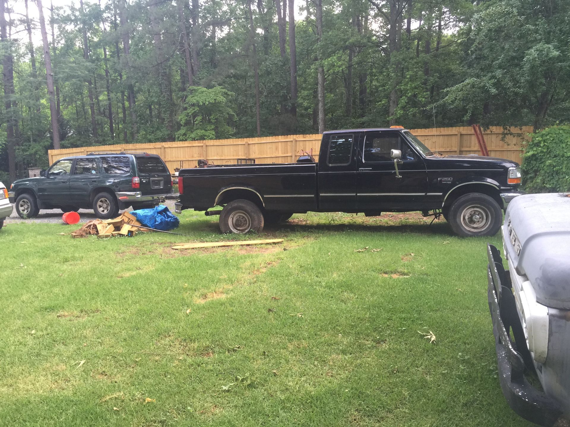 Black Ford pickup truck parked on grass, next to SUV and firewood. Wooden fence and trees in background.