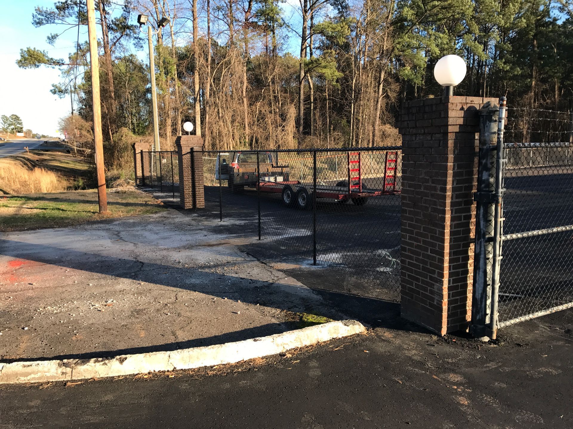 Black chain-link fence with brick pillars, trailer parked behind open gate, outdoor setting.