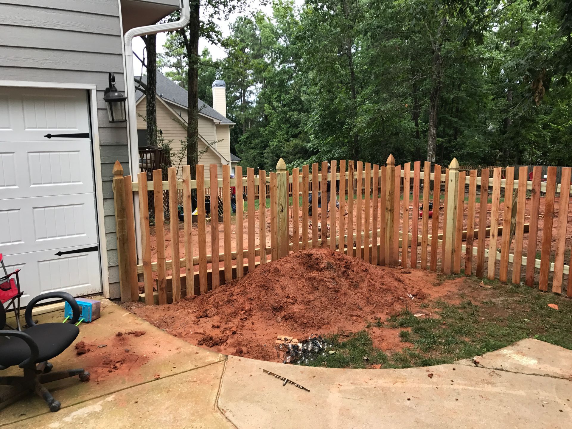 Brown wooden picket fence surrounds a pile of dirt next to a garage.