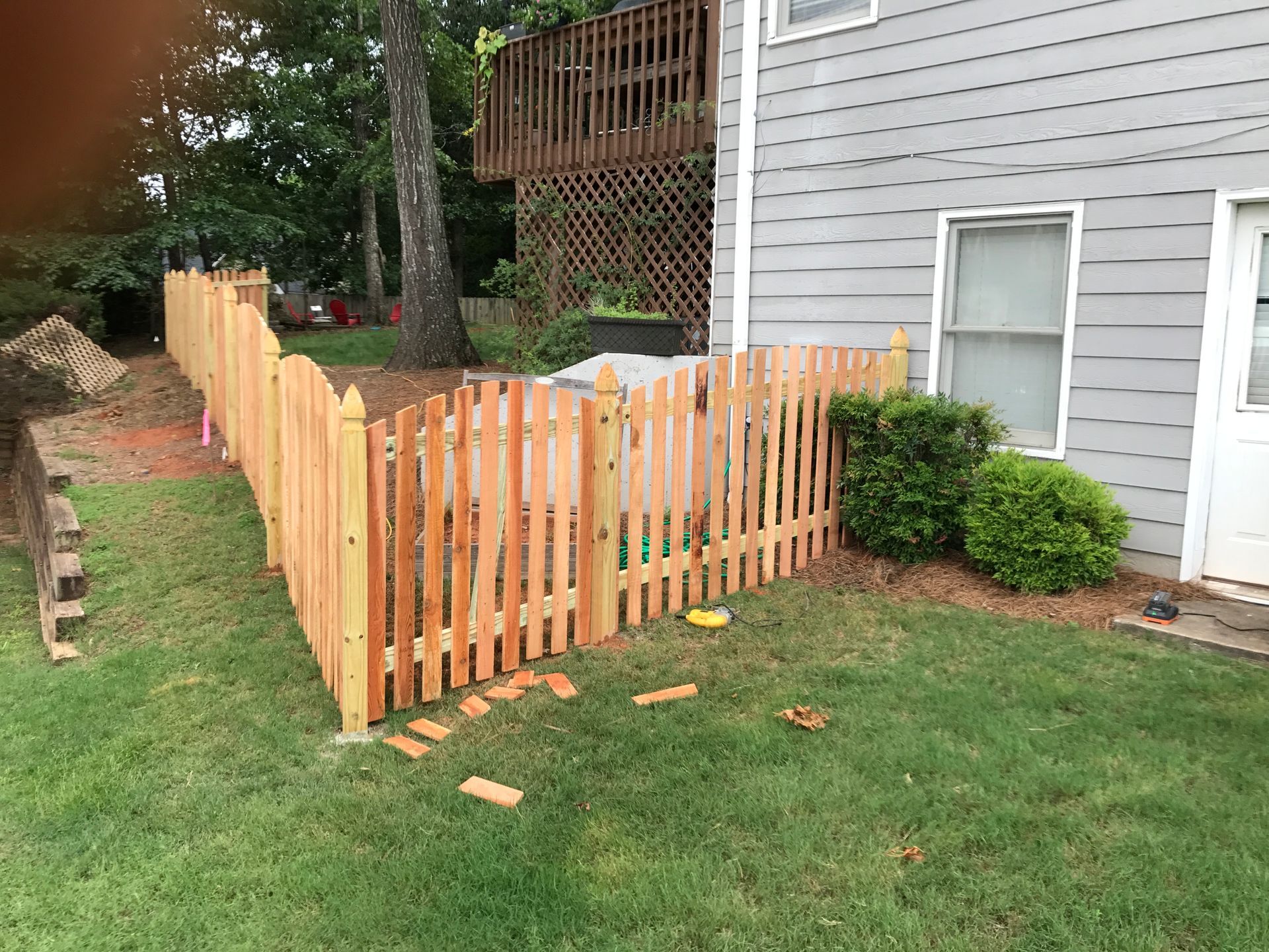 Wooden picket fence enclosing a grassy yard next to a gray building.