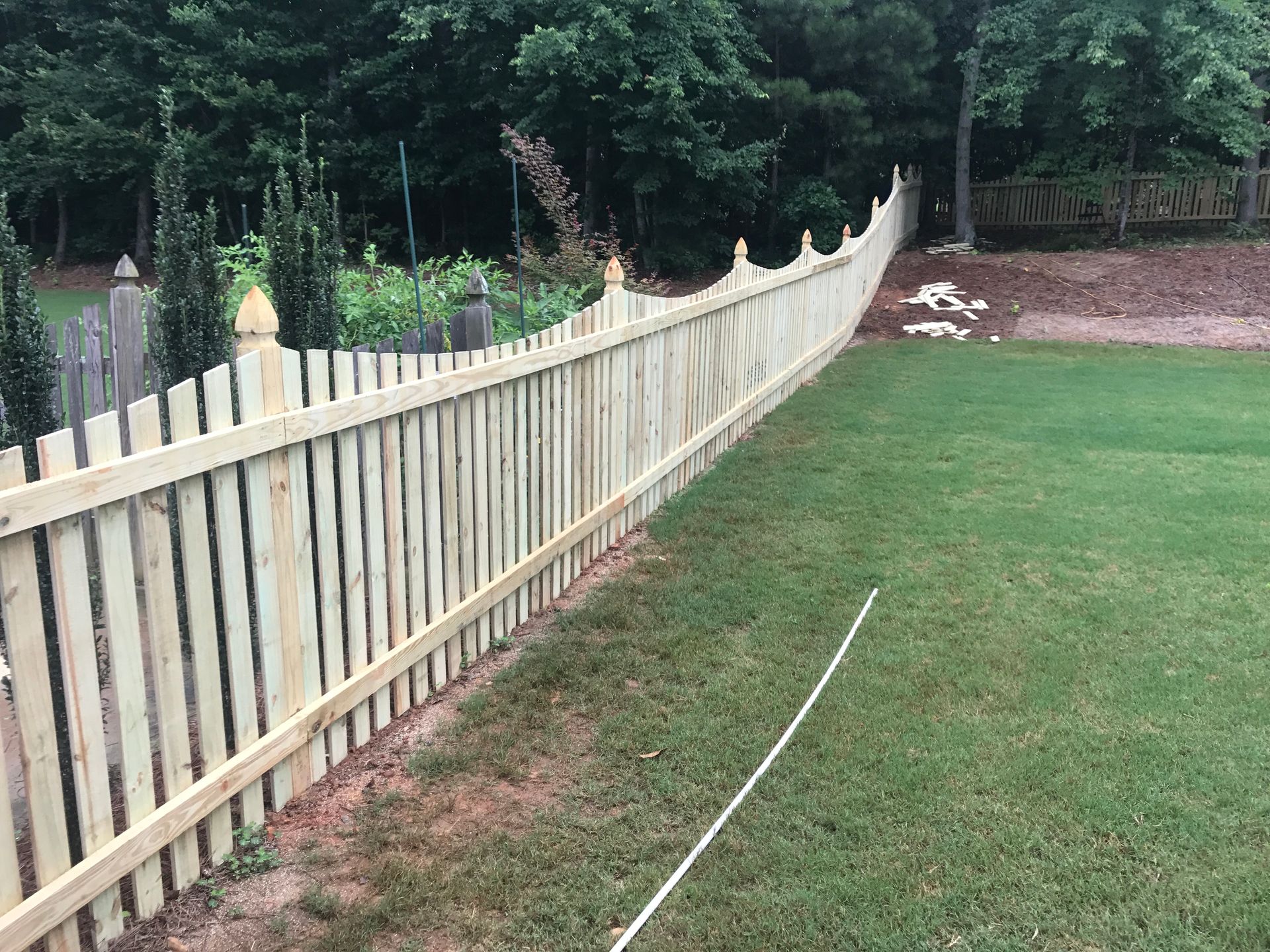 Wooden fence in a backyard with a grassy lawn, trees in the background.