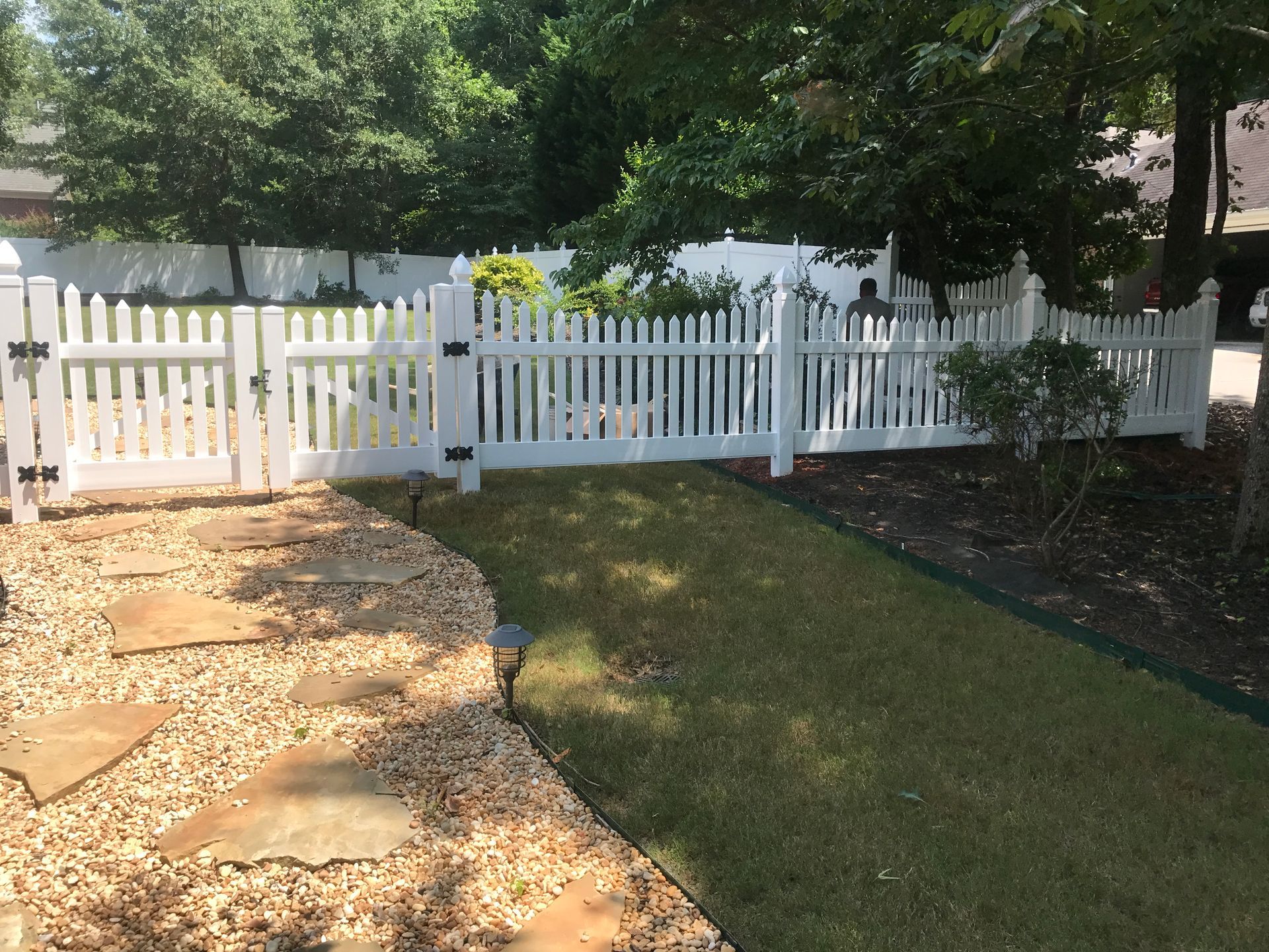 White picket fence surrounding a green lawn and stone pathway.
