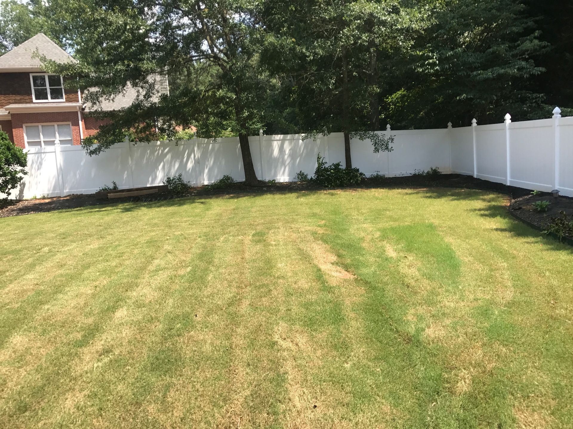 A white vinyl fence encloses a green lawn, with a house visible on the left and trees along the fence.