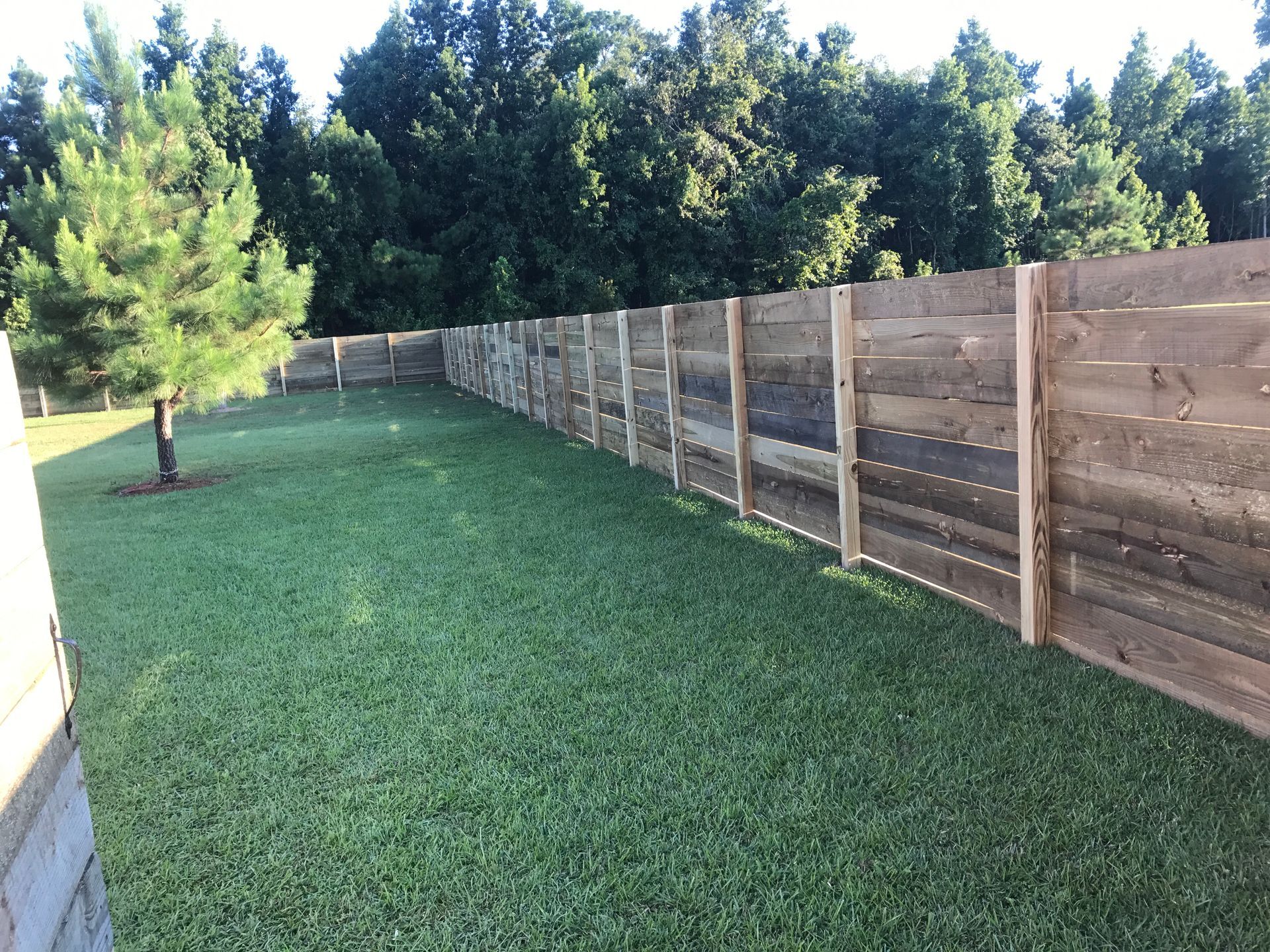 Wooden fence along green lawn, with trees in the background.