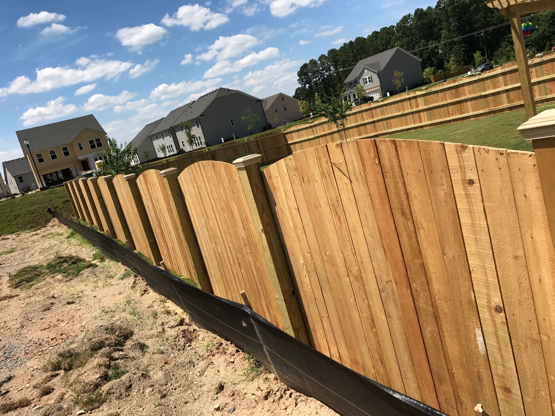 Wooden fence along a hillside, with houses and blue sky in the background.