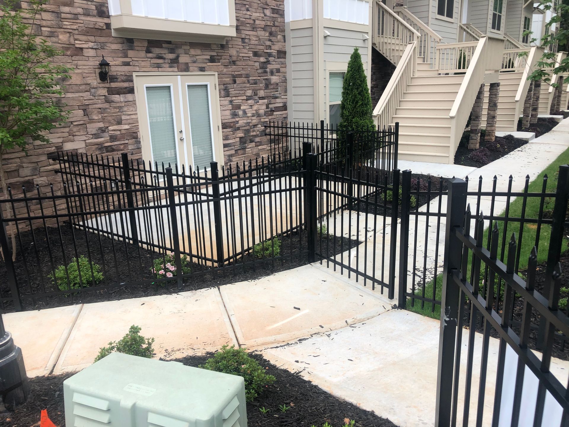 Black metal fence encloses a paved pathway near an apartment building.
