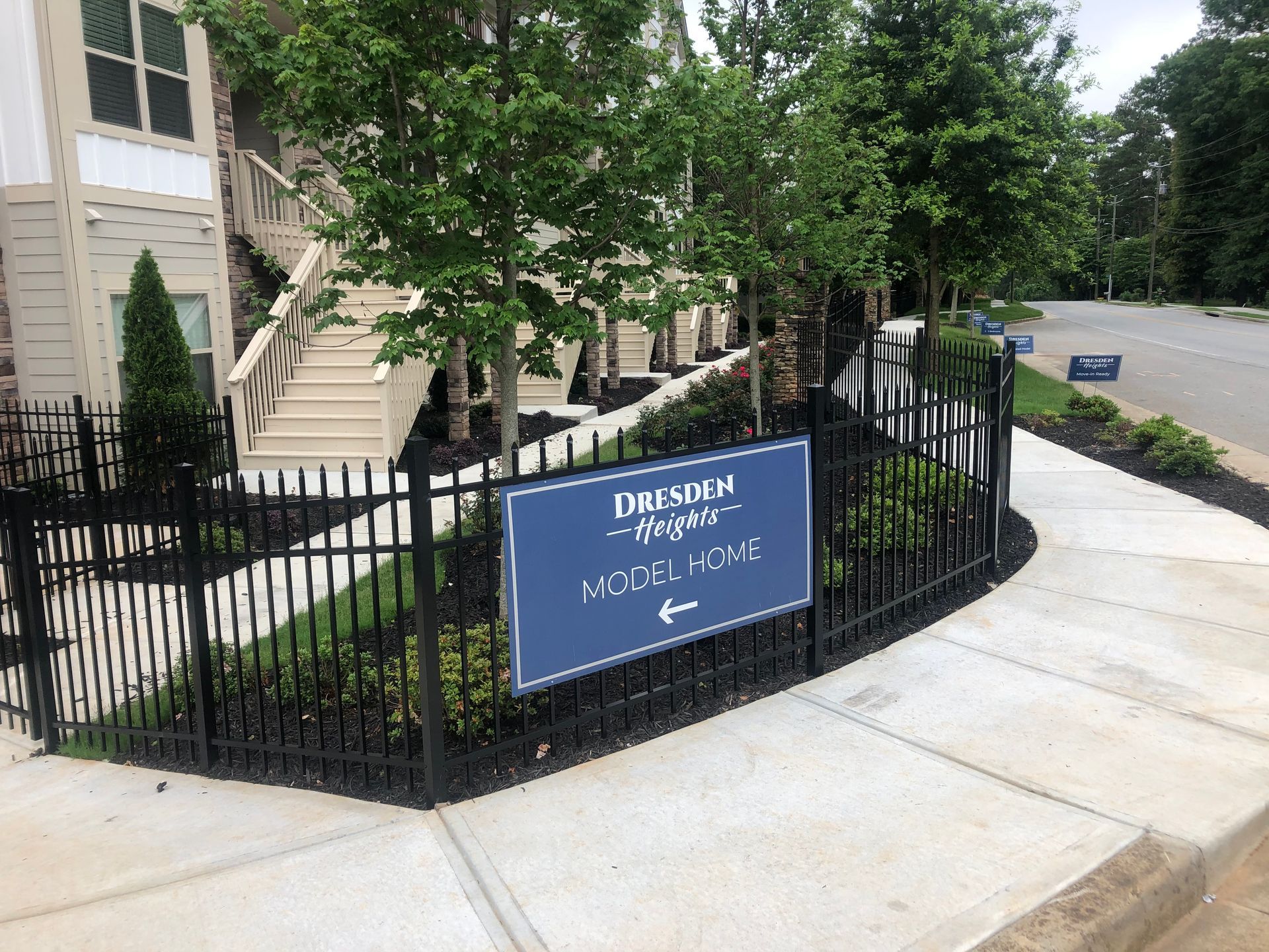 Sign for Premier Homes Model Home, black metal fence, sidewalk, landscaping, and building.