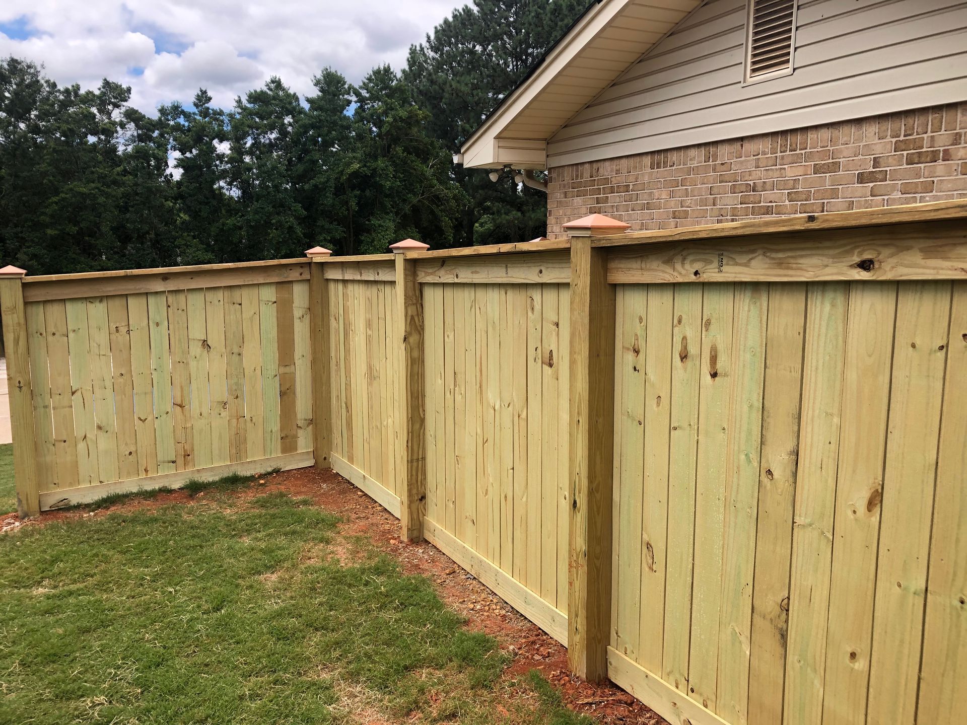 Wooden privacy fence along a green lawn beside a brick-sided house.