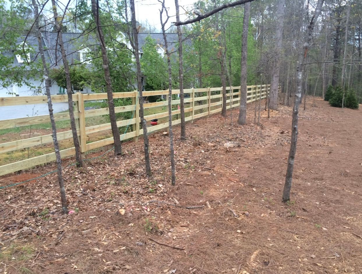 Wooden fence in a wooded area next to a house. Brown and green colors dominate.