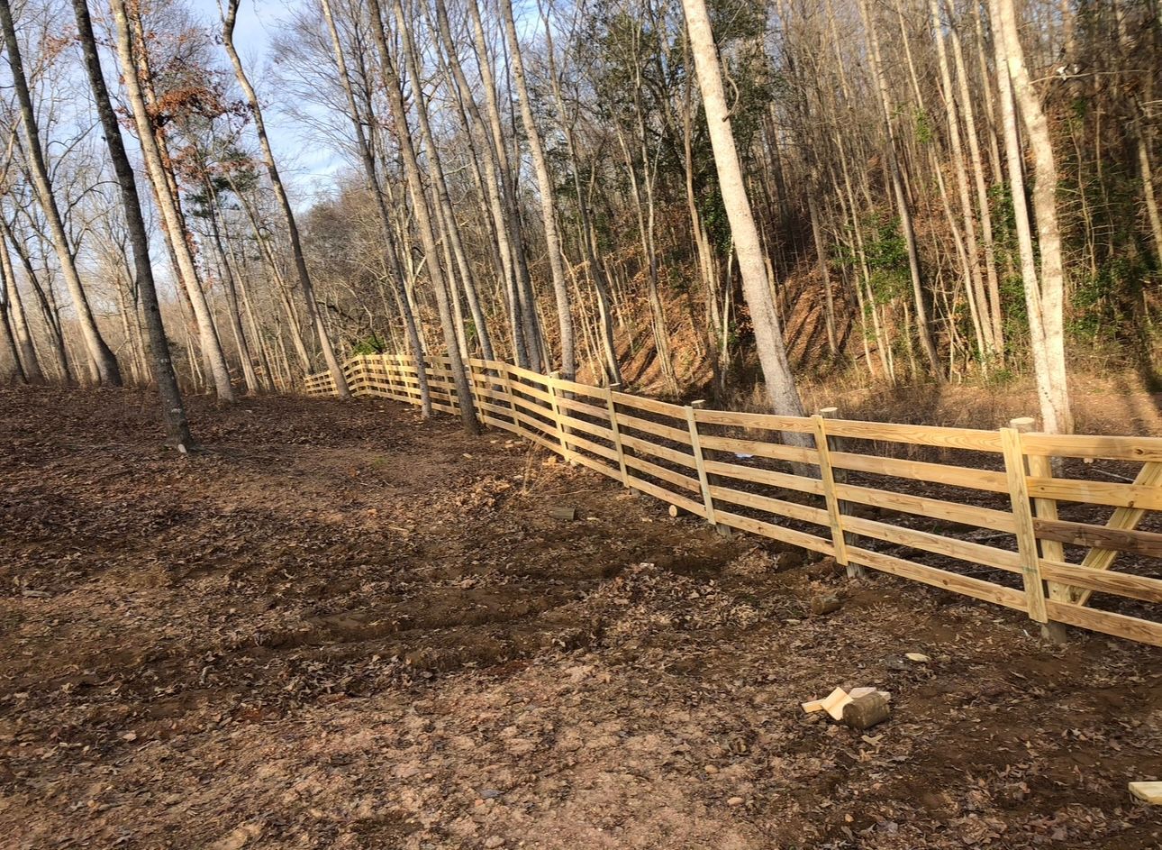 Wooden fence running through a wooded area with bare trees.