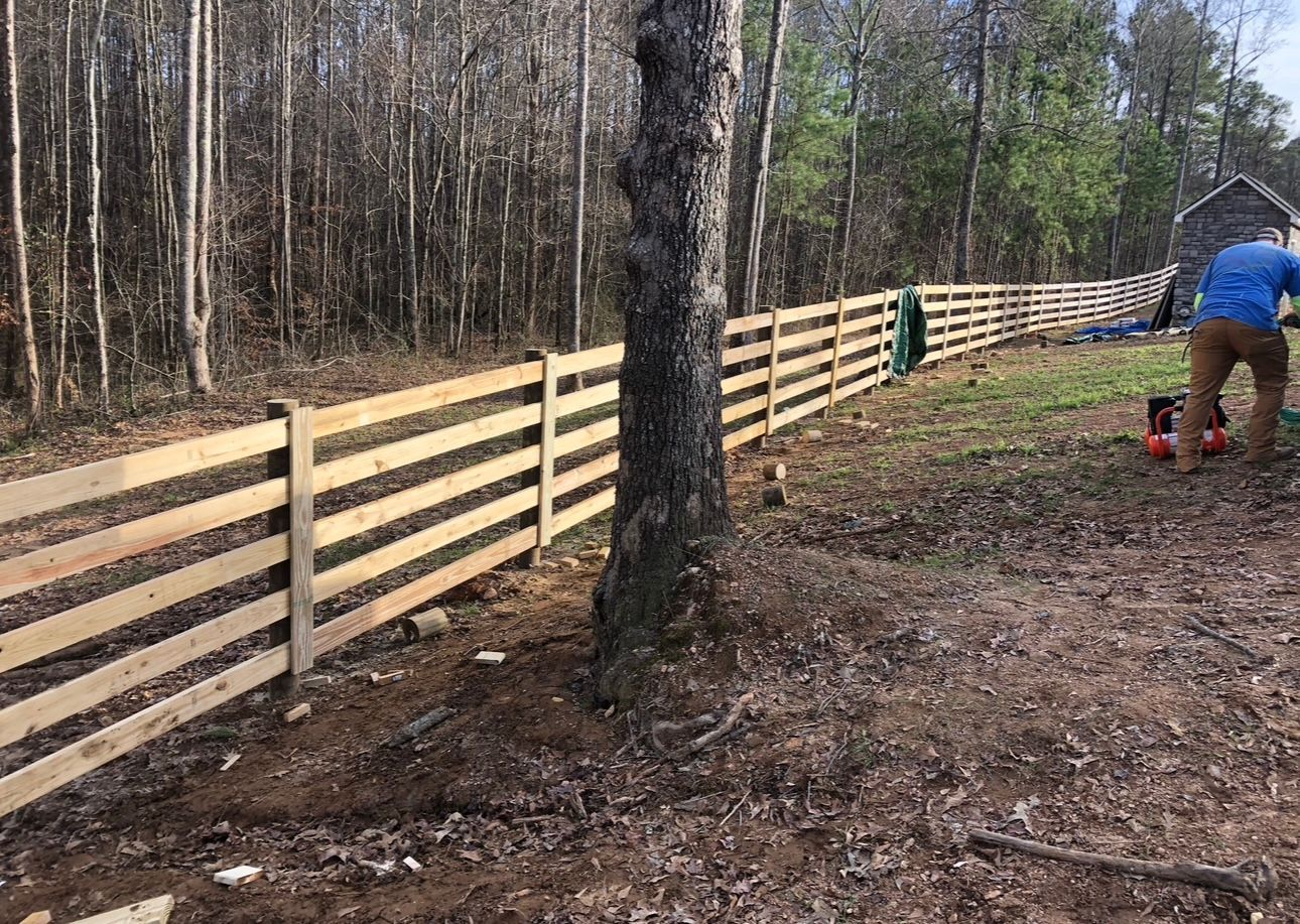 Wooden fence being built in a wooded area with a person working on the right side.