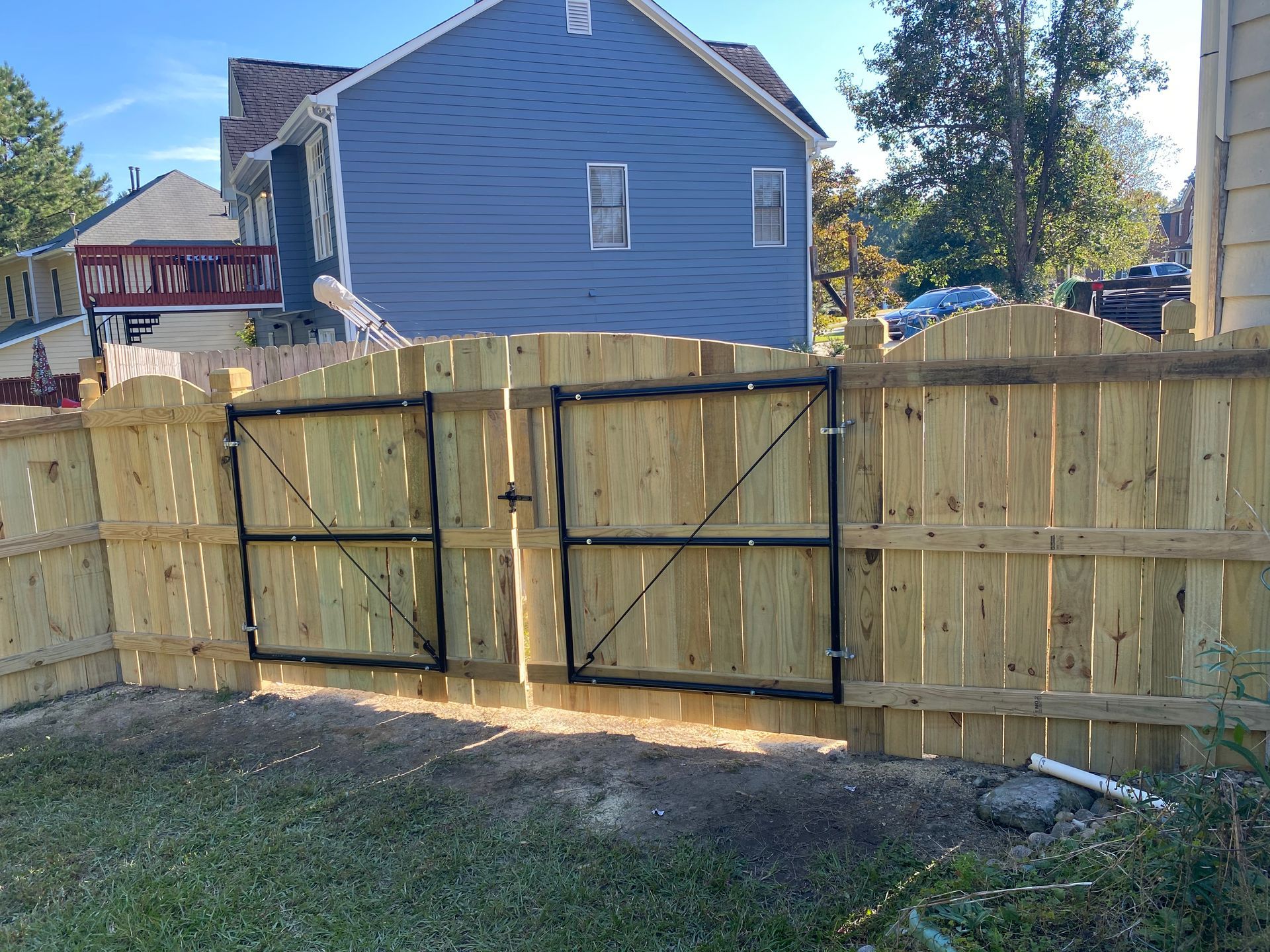 Wooden fence with black metal gates in front of a blue house.