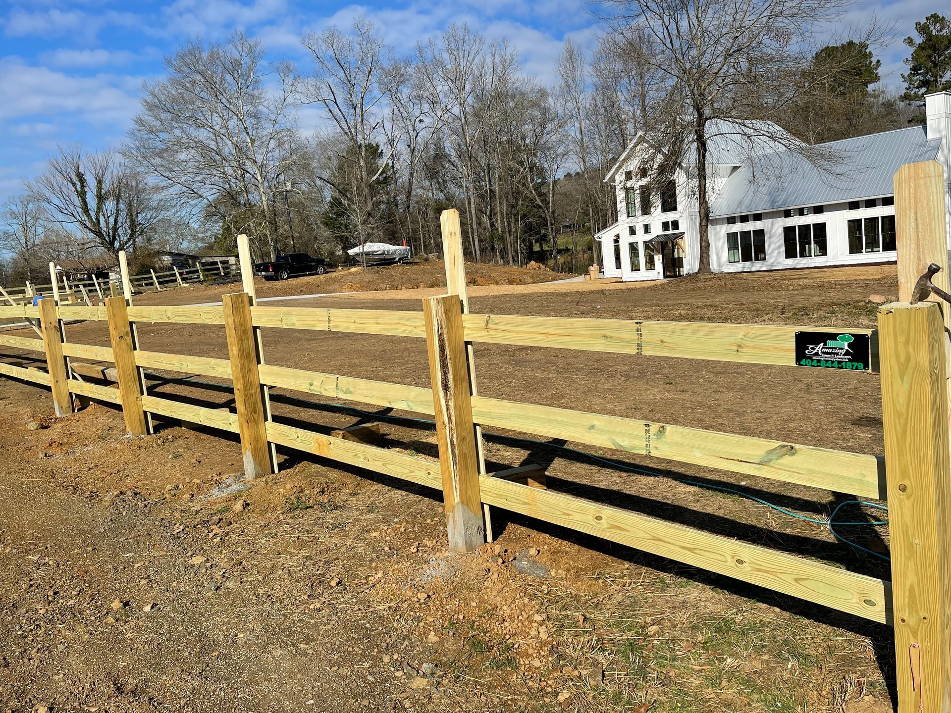Wooden fence in front of a white house with bare trees in the background under a blue sky.