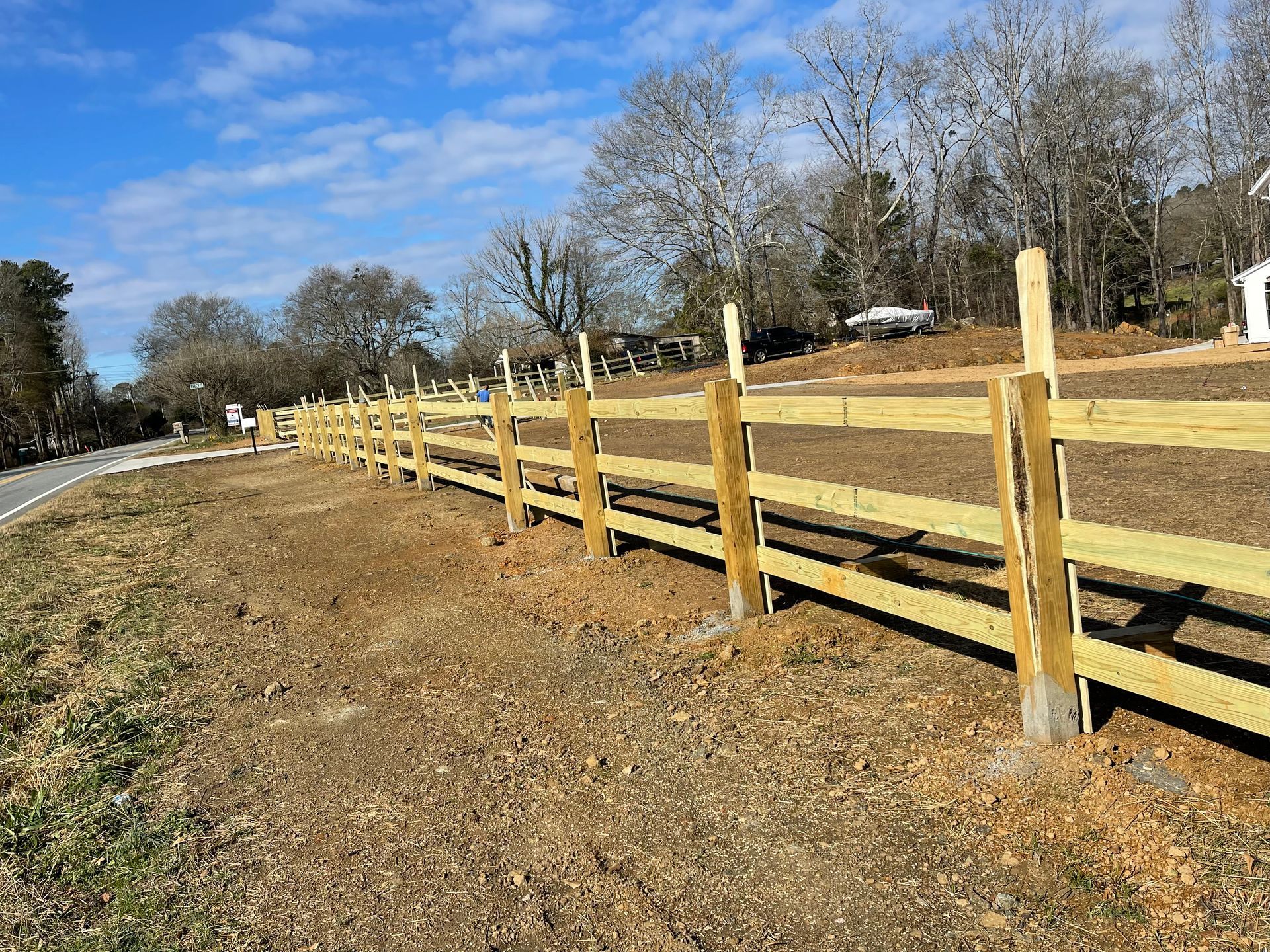 Wooden fence along a roadside, bright blue sky, trees in the background.