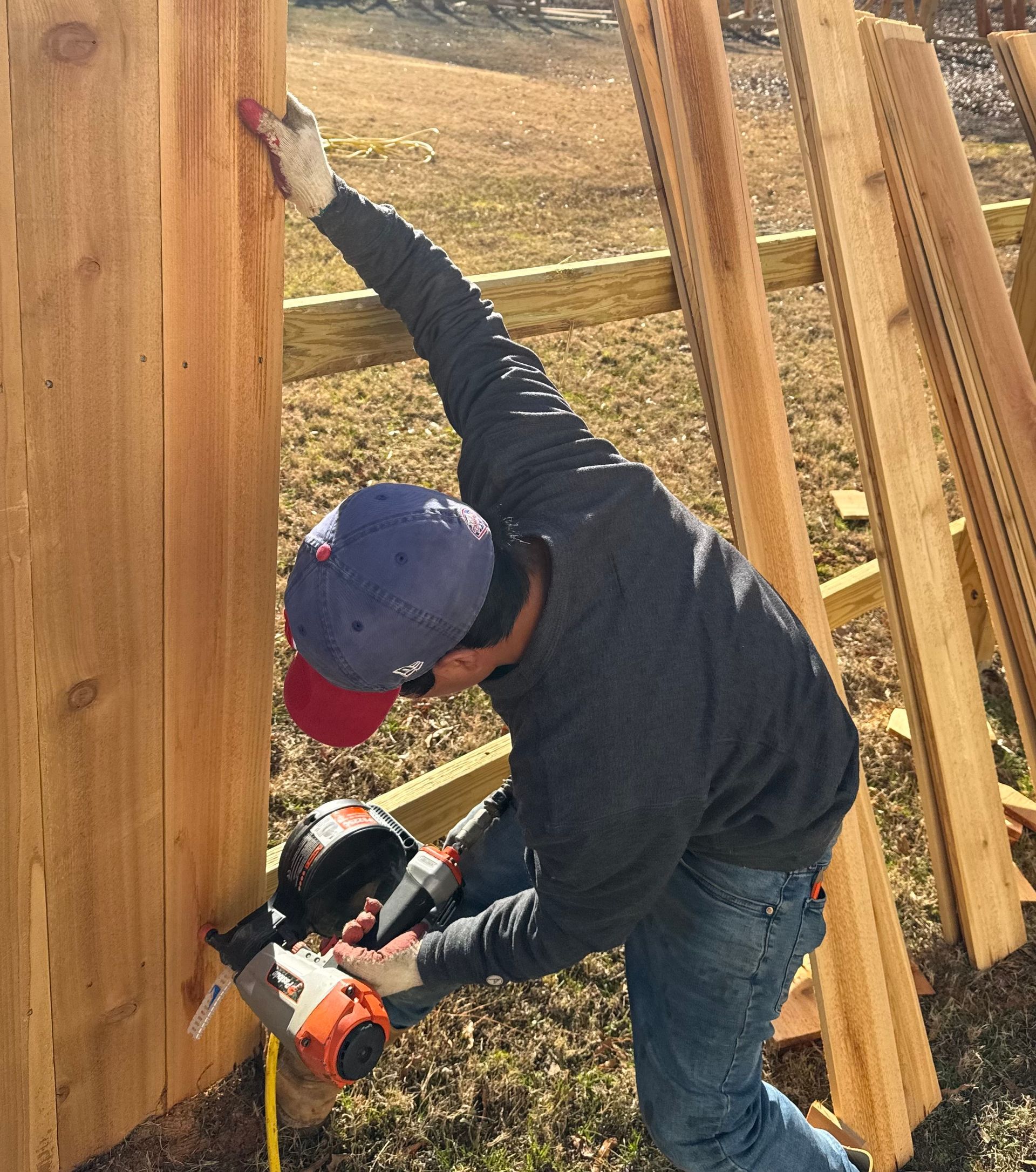 Person using a nail gun to attach wooden planks to a fence post outdoors.