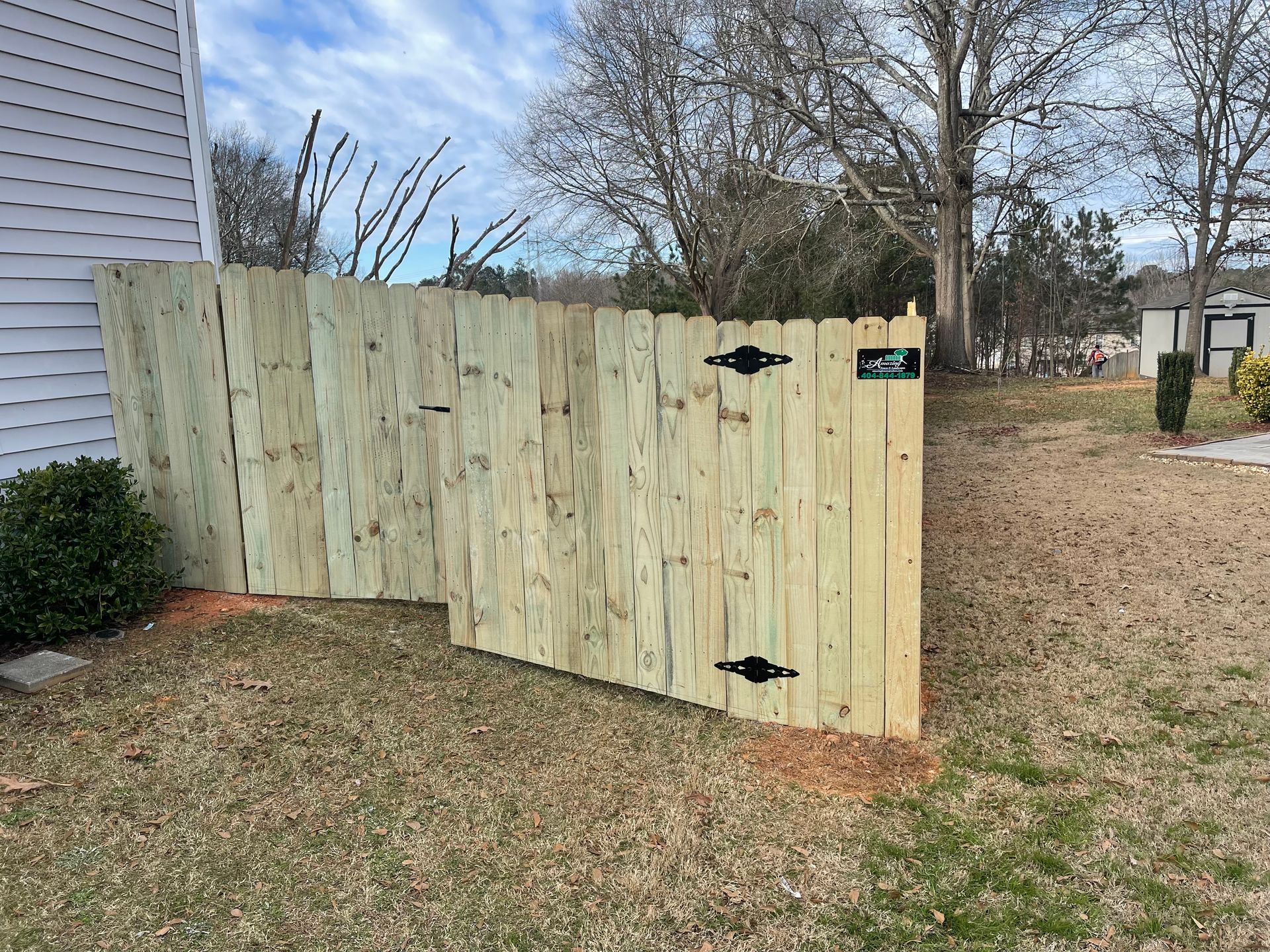 Wooden fence with gate in yard, next to a building and some landscaping.