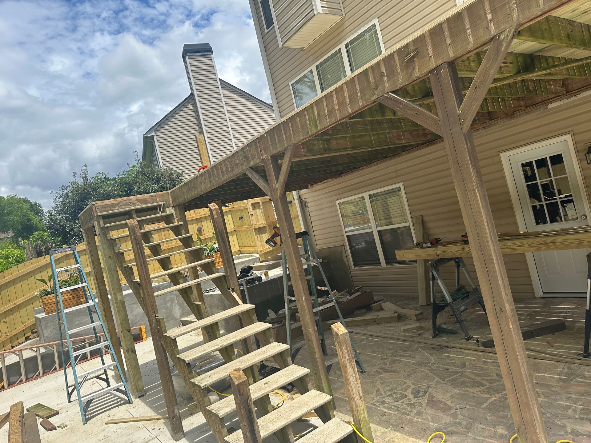 Wooden deck with stairs leading down to a concrete patio area, attached to a light brown building.