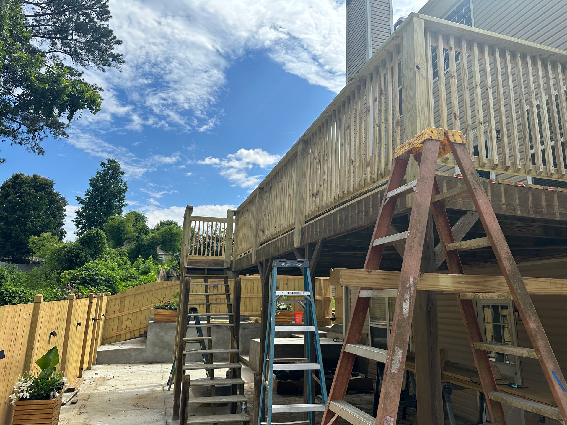Wooden deck under construction with ladders and a clear sky.