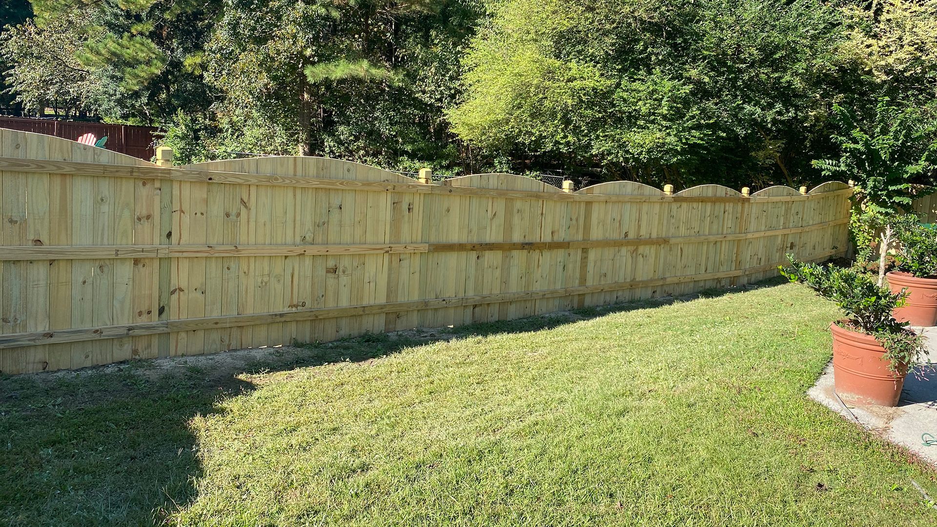 Wooden fence bordering a green lawn, with trees in the background.