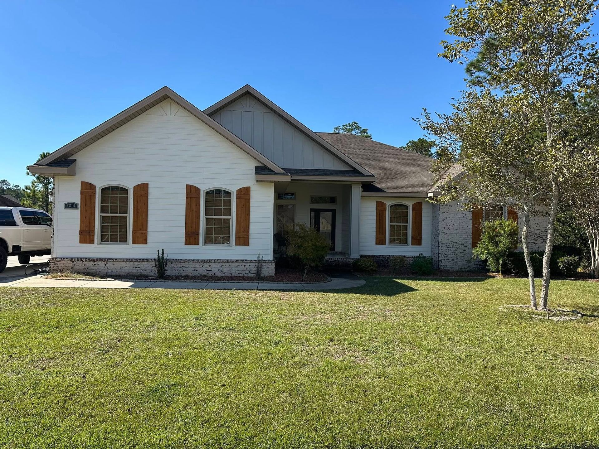 White house with brown shutters, gray roof, and green lawn under a blue sky.