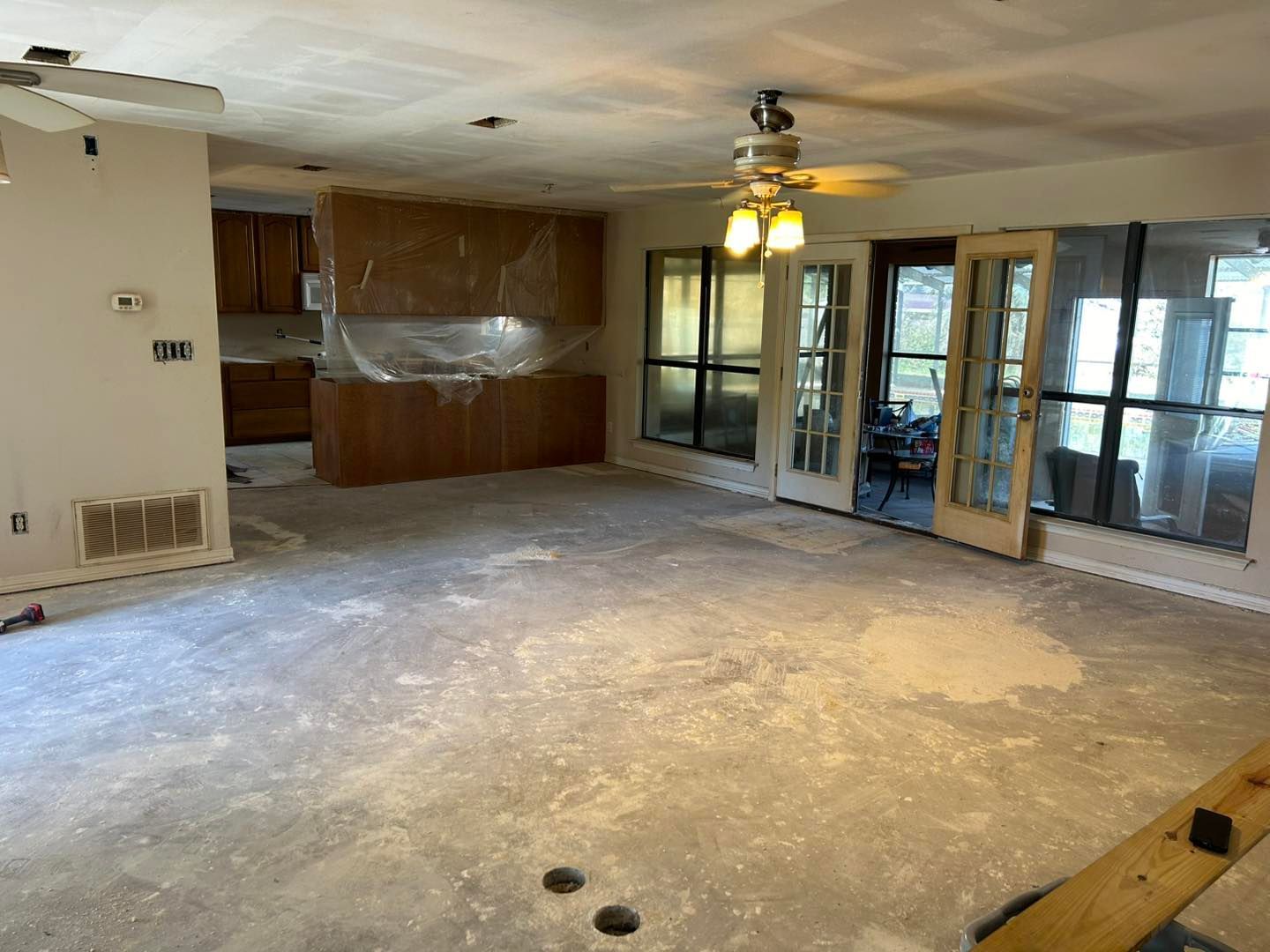 Interior room under renovation, with exposed floor, cabinets, French doors, and ceiling fan.