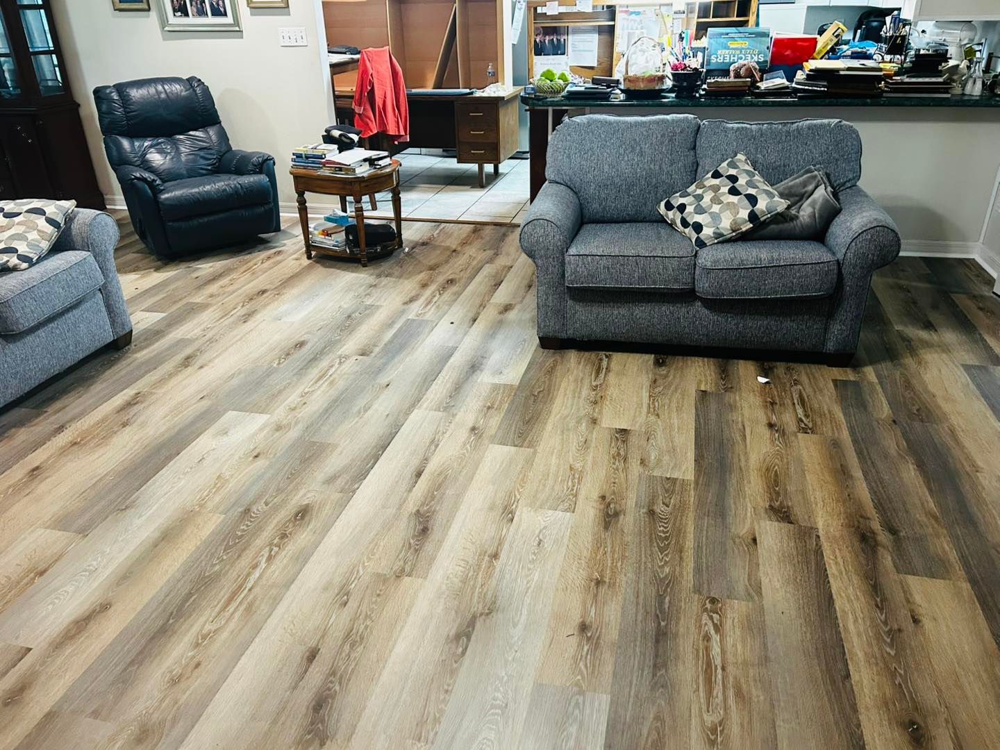 Living room with wood-look flooring, gray couches, a black recliner, and a round table.