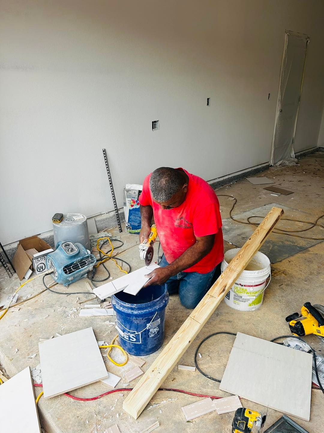 Man cutting tile with a power saw, surrounded by tools and construction materials.