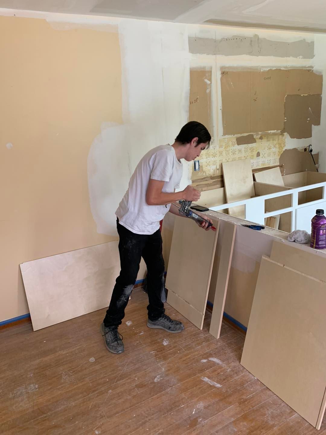Person in a white shirt and black pants works on wood panels in a room under renovation.