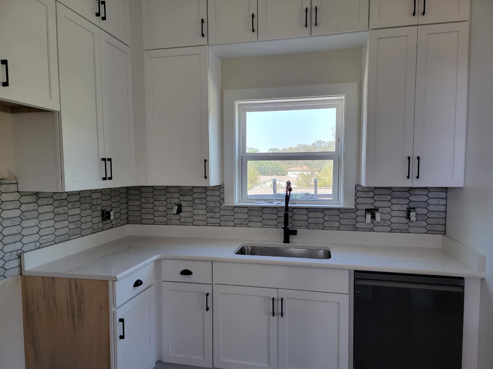 White kitchen with light countertops, black cabinet pulls, and a window above the sink.