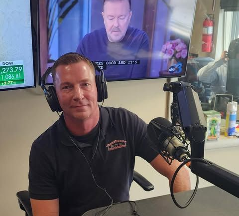 Man in a recording studio with headphones, microphone, and a TV screen.