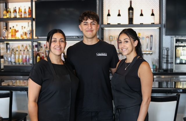 Three restaurant staff members smiling behind a bar.