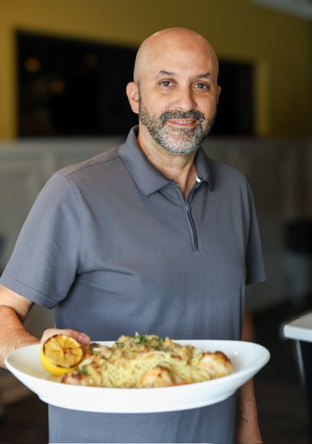 Man holding a plate of food, smiling. He is in a restaurant.