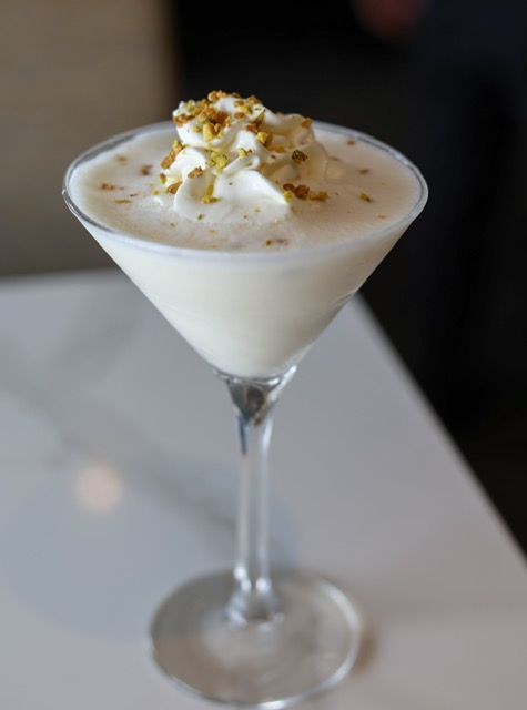 Creamy cocktail in a martini glass, garnished with whipped cream and crushed pistachios.