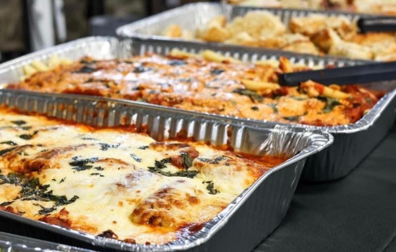 Aluminum foil pans filled with lasagna and other food on a table.