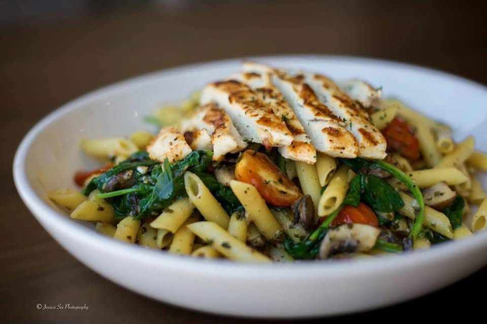A white bowl filled with pasta and chicken on a wooden table