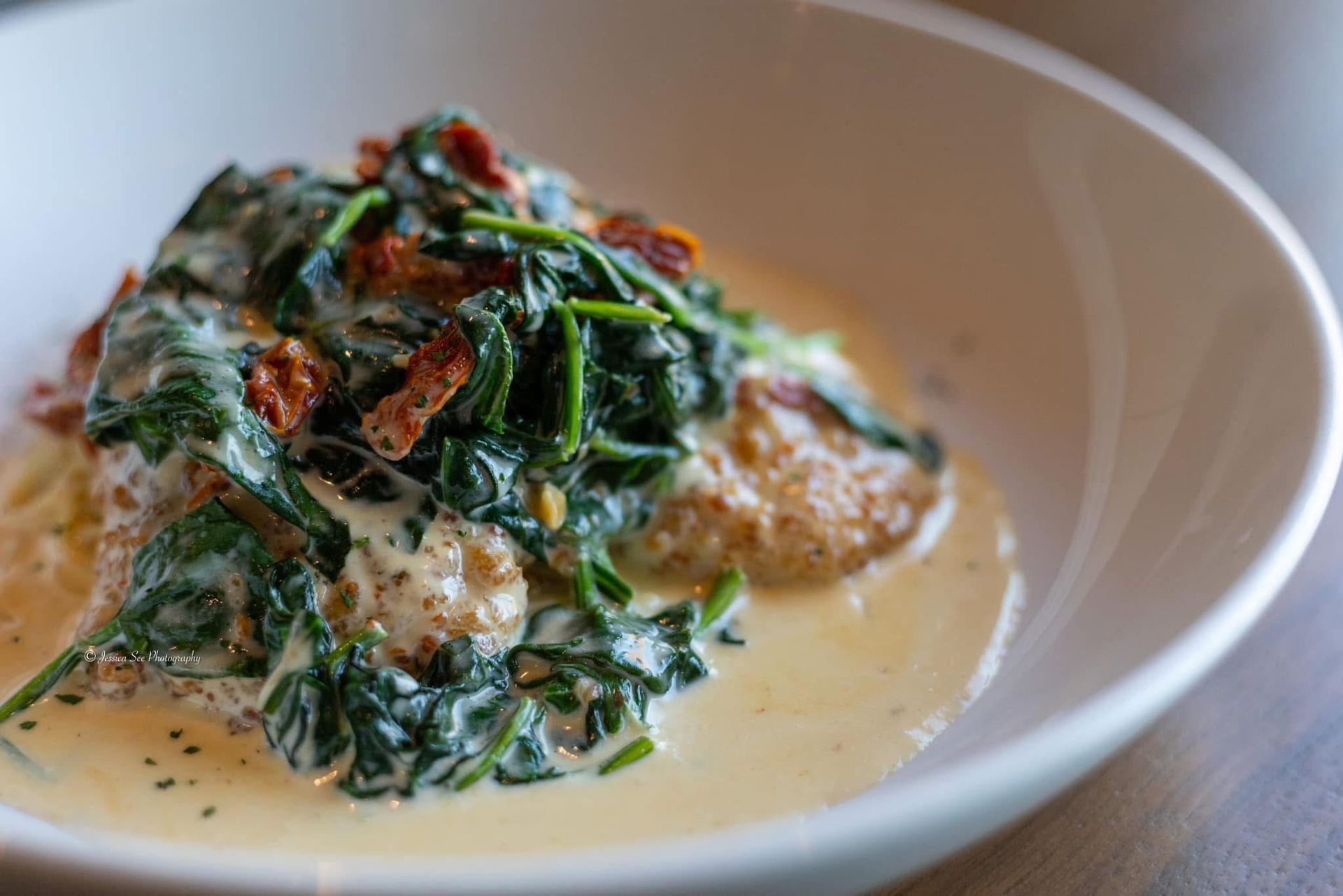 A white bowl filled with spinach and meatballs in a creamy sauce