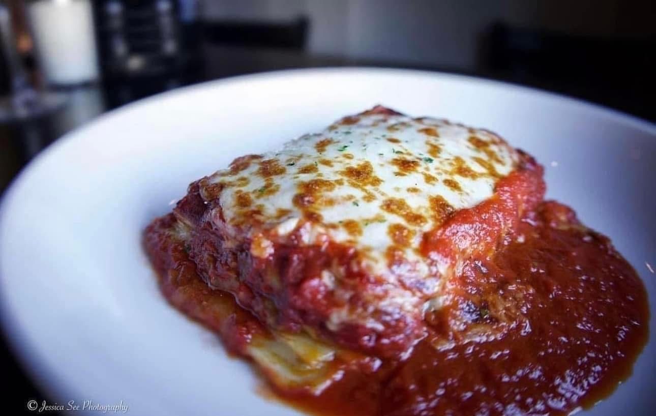 A white plate topped with a lasagna covered in sauce and cheese