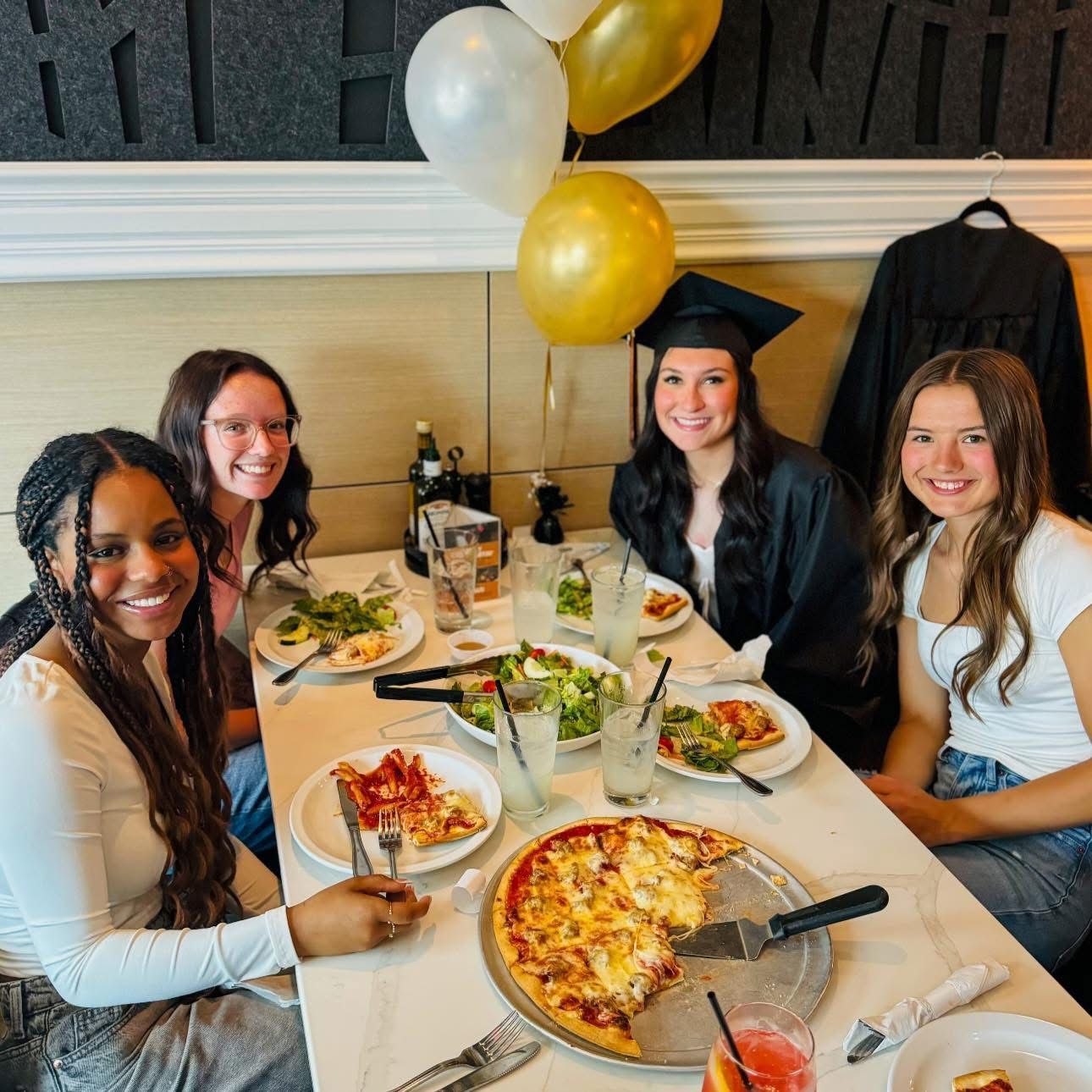 A group of women are sitting at a table with plates of food and balloons.