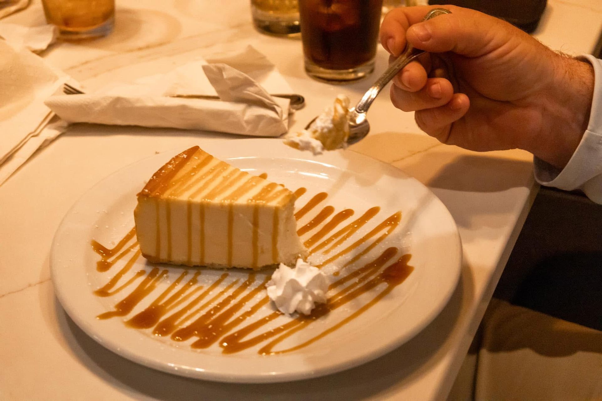 A person is eating a slice of cheesecake with whipped cream and caramel sauce