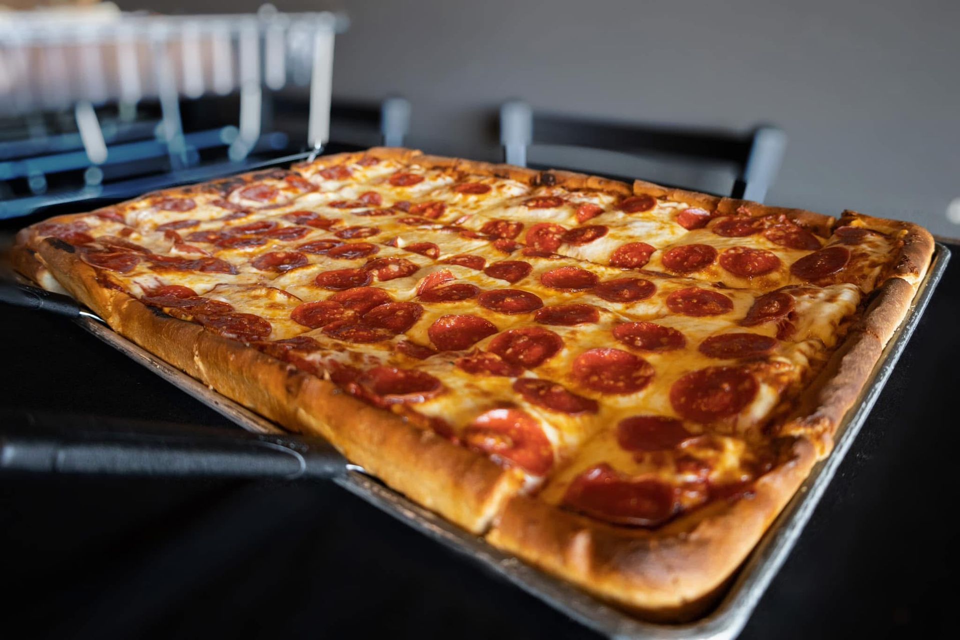 A large pepperoni pizza is sitting on a pan on a table