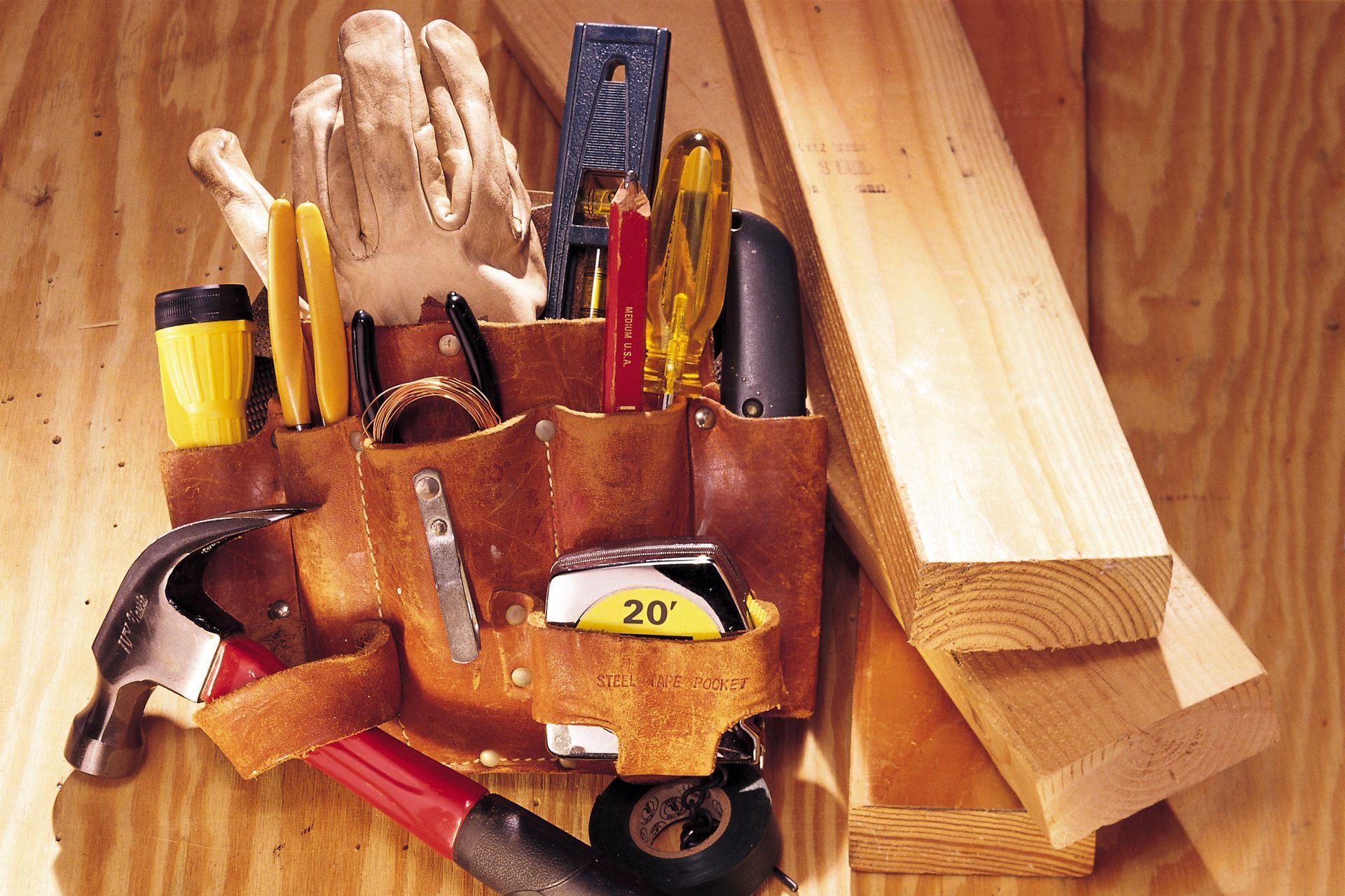 Tool belt with tools, wood planks, and work gloves against a wooden background.