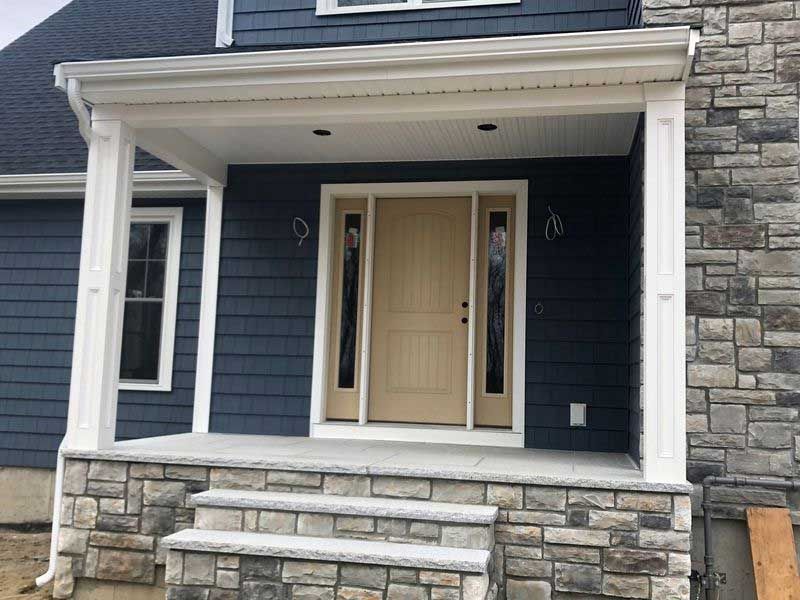 Blue house with stone porch and columns; tan door, steps.