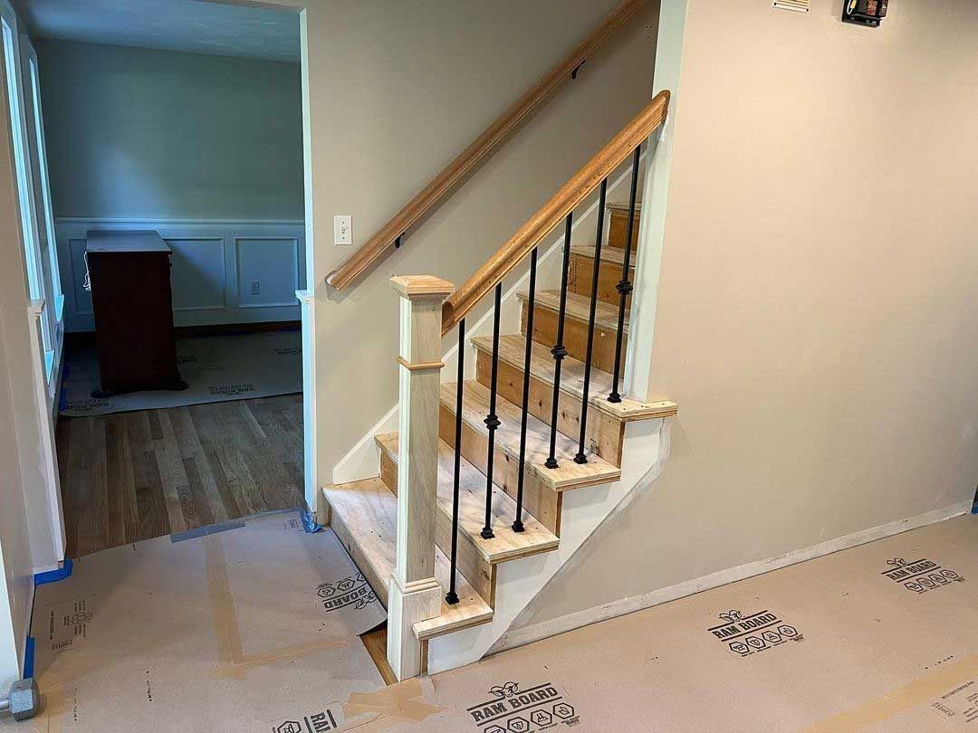 Staircase with wooden handrail, black iron spindles, and beige walls. The stairs are located near an open doorway.