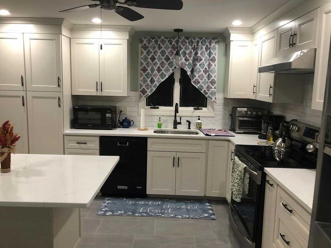 White kitchen with black appliances, island, and patterned curtain.