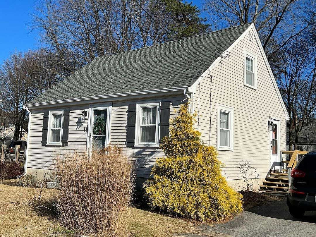 Small beige house with gray roof and a yellow bush in front.