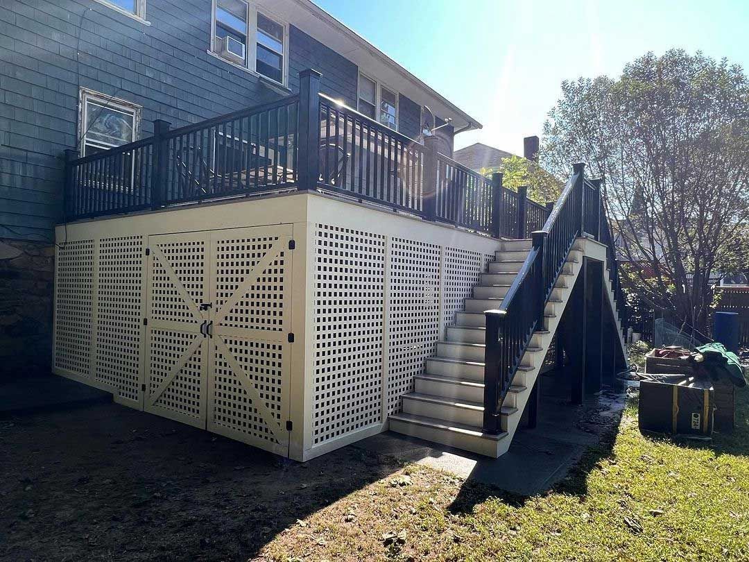 White lattice deck skirt with dark railing, stairs, and house, in an outdoor setting.