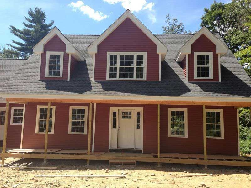 Red house with white trim, front porch, and three dormers under blue sky.