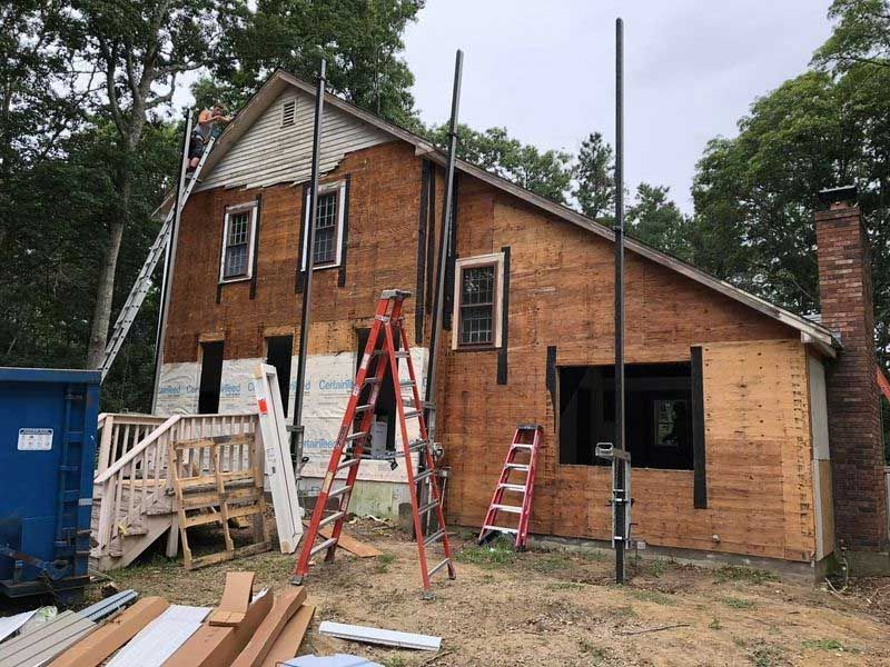 House under construction; wood siding exposed, scaffolding and ladders, blue dumpster.